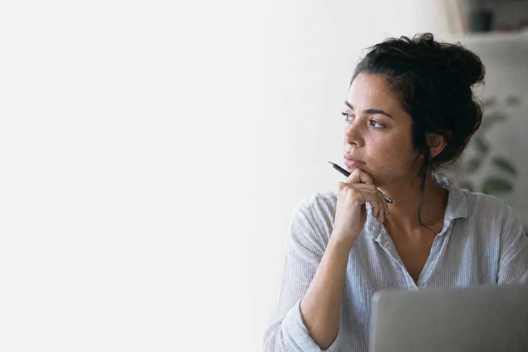 Mujer pensativa en su entorno de trabajo, mirando lejos de la pantalla en un momento de reflexión